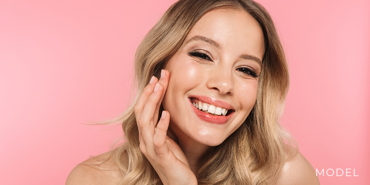 Model Gently Touching Her Cheek Against Pink Background