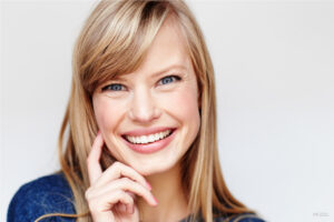 Smiling blond female touching cheek | perri dermatology