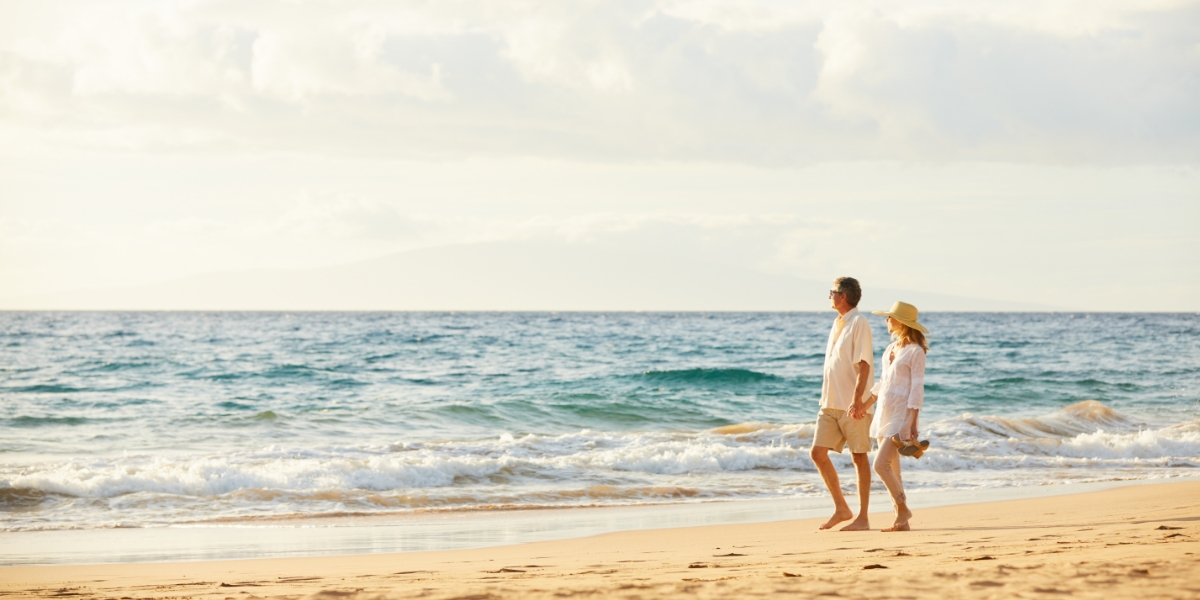 Model couple holding hands in sunshine walking along the beach | perri dermatology